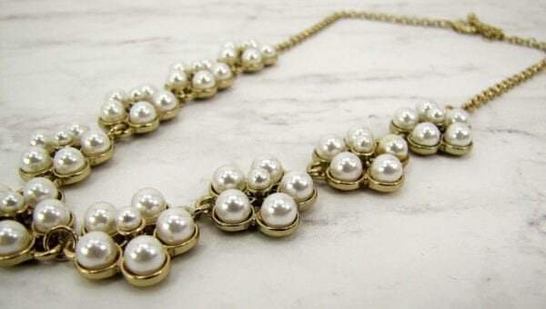 gold necklace with pearls arranged like flowers on a marble surface