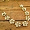 gold necklace with pearls arranged like flowers on a wooden surface