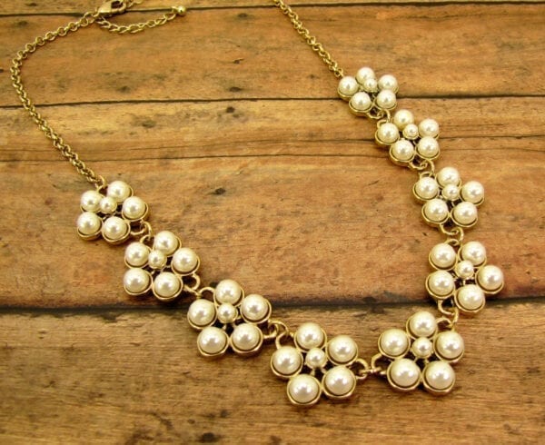 gold necklace with pearls arranged like flowers on a wooden surface