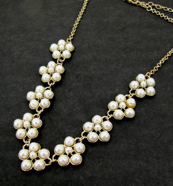 gold necklace with pearls arranged like flowers on a black velvet surface