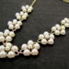 gold necklace with pearls arranged like flowers displayed on a black velvet surface