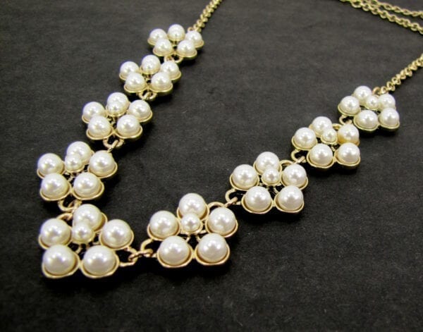 gold necklace with pearls arranged like flowers displayed on a black velvet surface