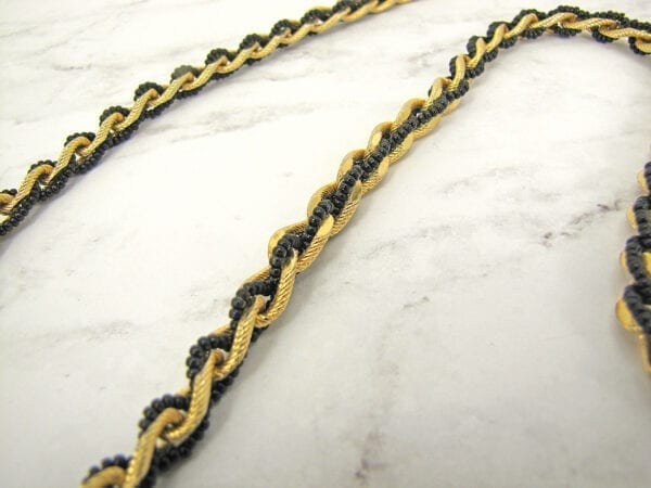 twisted necklace with gold chain and black pearls on a marble surface