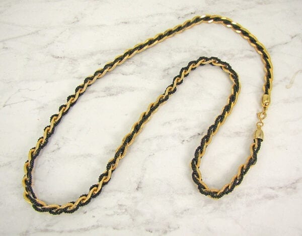 twisted necklace with gold chain links and black pearls on a marble surface