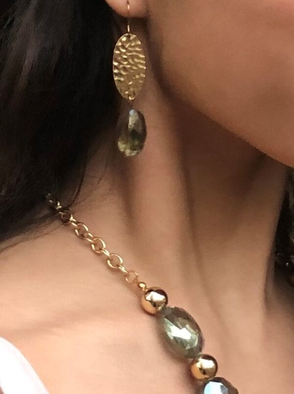 close up of a girl wearing earrings with gold beads and olive-green crystals