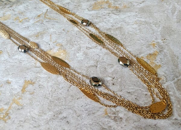 layered necklace with gold chains and large gold bands on a concrete surface