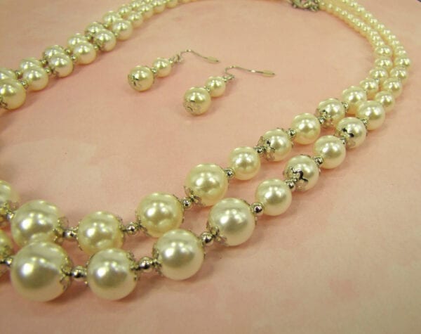 pearl earrings and layered necklace on a light pink surface