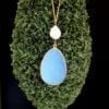 golden necklace with large white stone pendant on a green moss surface