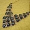 geometric necklace with dark teardrop crystals on a dark yellow surface