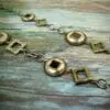 segment of a silver chain necklace with metal beads shaped like square and circles on a wooden surface