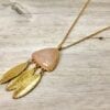 pink, triangular necklace pendant with hanging feathers on light brown wooden surface