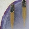 earrings with hanging golden chains and rectangular pendants on a violet surface