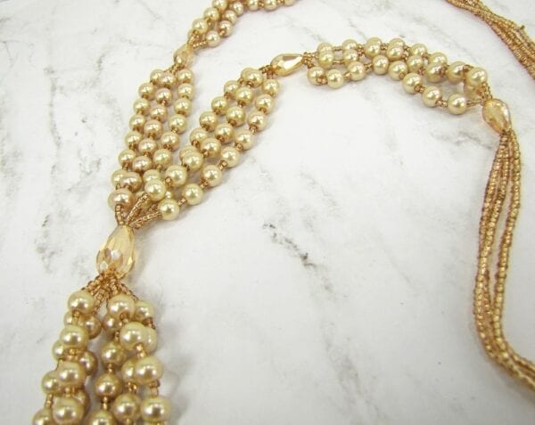 close up of a knotted golden necklace with pearl inlays on a marble surface