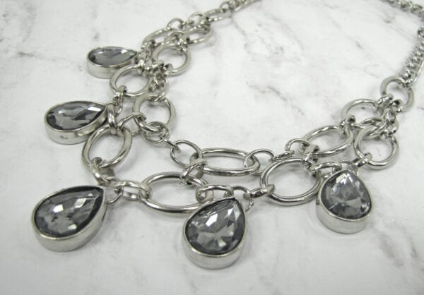 close up of a necklace with silver chain links and smoky gray gems on a marble surface