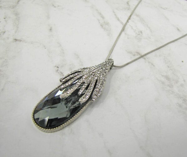 necklace pendant with black oval crystal and diamond filigree on a marble surface