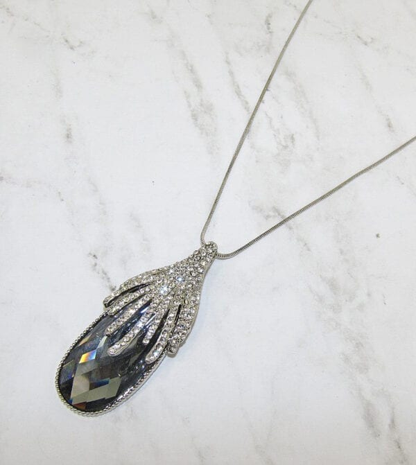necklace with black oval crystal and diamond filigree on a marble surface