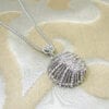necklace with silver pendant with wing segment design on a brown cloth surface