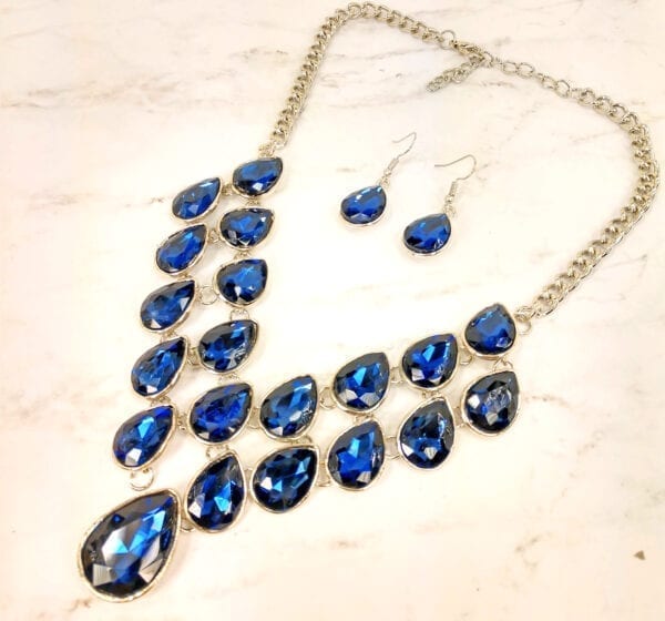 silver chain necklace with many blue teardrop sapphires on a marble surface