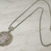 necklace with silver pendant with wing segment design on a marble surface