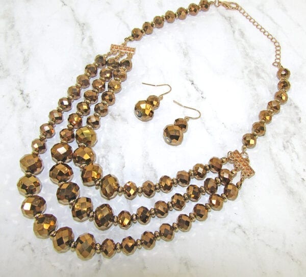 layered necklace and earrings with golden beadwork on a marble surface