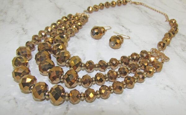 layered necklace and earrings with golden beads on a marble surface