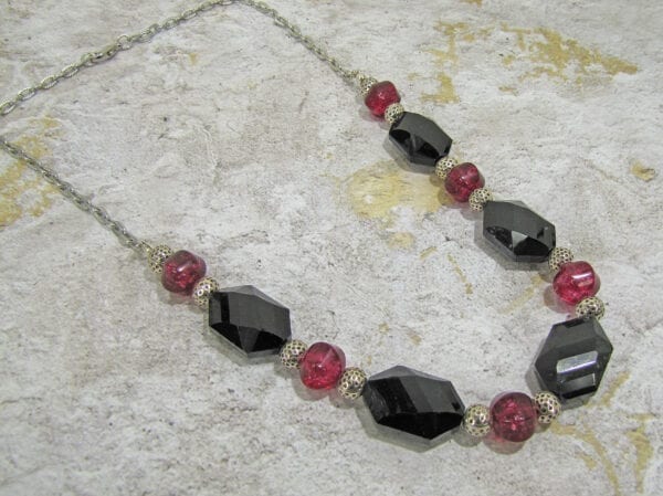 necklace with hexagonal black crystals and ruby beads on a concrete surface