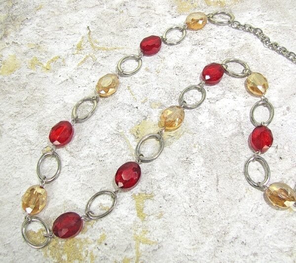 necklace with red and yellow crystals and silver chain hoops on a concrete surface