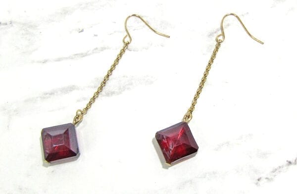 earrings with long chains and red square gems on marble surface