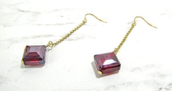 earrings with long chains and red square gemstones on marble surface