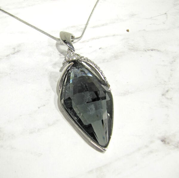 necklace pendant with black gem and metal filigree on a marble surface