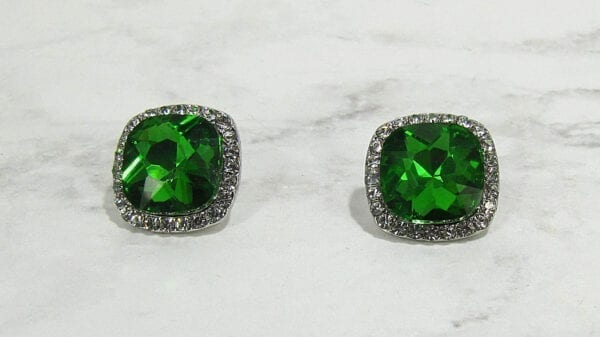 front view of stud earrings with square cut green gems on a marble surface