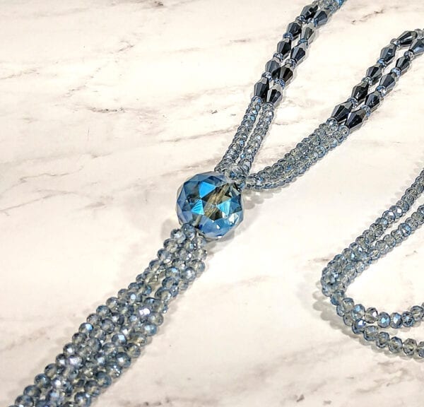 close up of a crystal necklace with large blue gem pendant on a marble surface