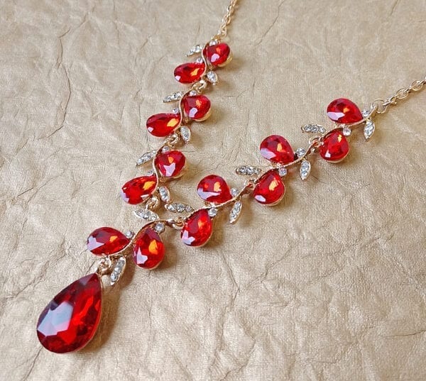 gold necklace with teardrop ruby gems arranged like a vine on shimmering surface