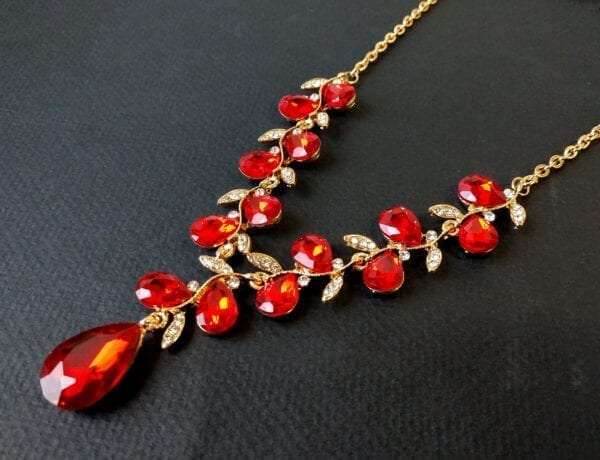 gold necklace with teardrop ruby gems arranged like a vine on matte black surface