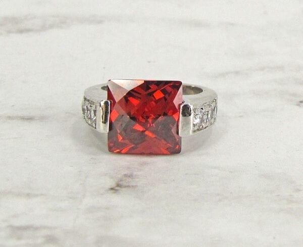 front view of a ring with square-cut garnet gem on a marble surface