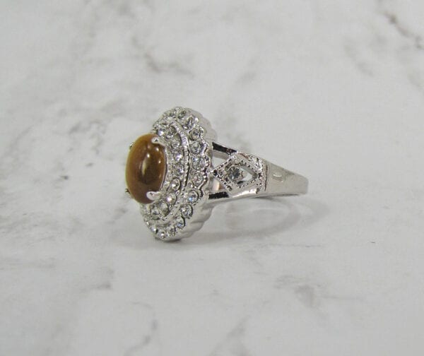 side view of a ring with polished oval brown gem on marble surface