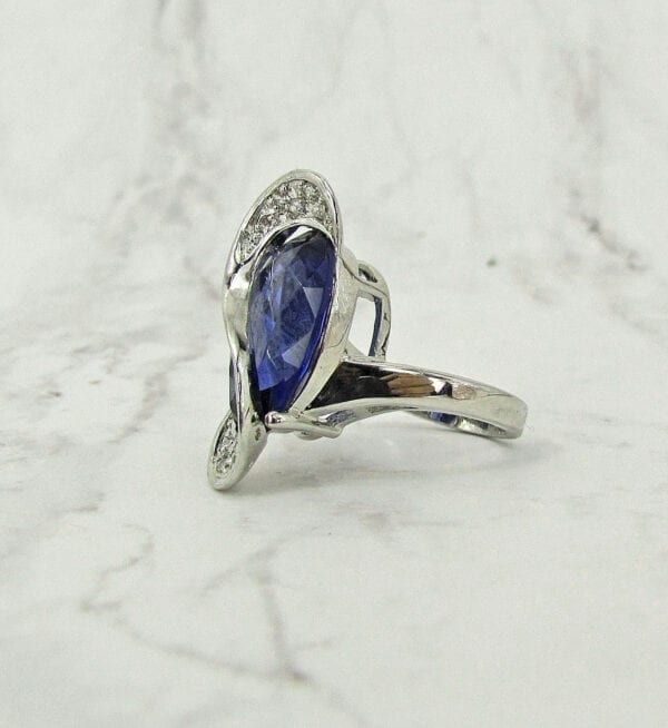 side view of a ring with blue gem and s-shaped design on marble surface