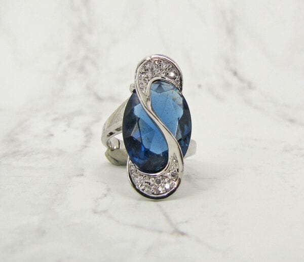 front view of a ring with blue gem and s-shaped design on marble surface