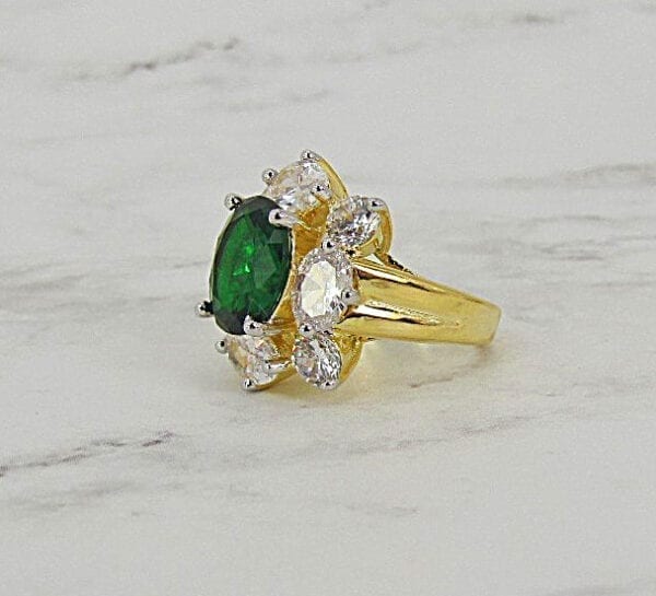 ring with large oval emerald gem surrounded by white crystals on marble surface