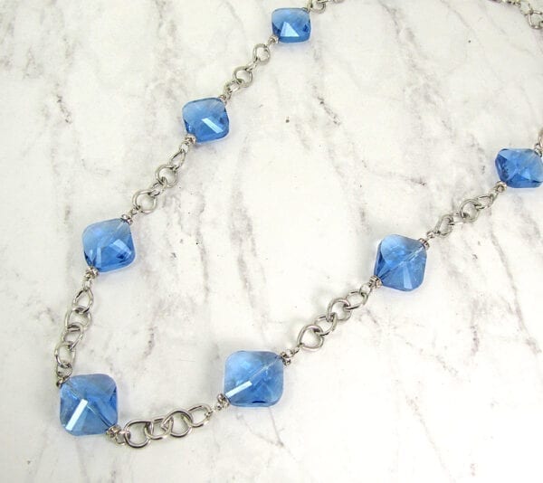 top view of a silver chain necklace with light blue gemstones on marble stones