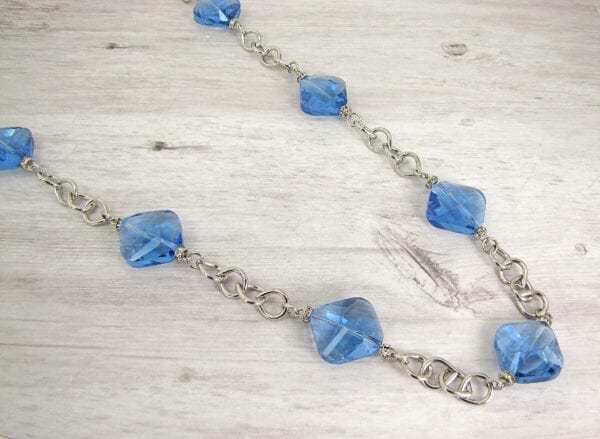 silver chain necklace with light blue gemstones on a wooden necklace