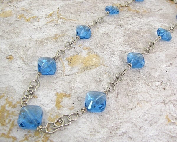 silver chain necklace with light blue gemstones on a concrete necklace