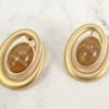 golden earrings with brown gem on the center on a marble surface