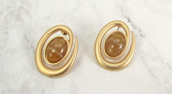 golden earrings with brown gem on the center on a marble surface