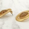 golden earrings with brown gem on the center laid sideways on a marble surface