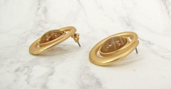 golden earrings with brown gem on the center laid sideways on a marble surface