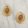 golden earrings with brown gemstone on the center on a marble surface
