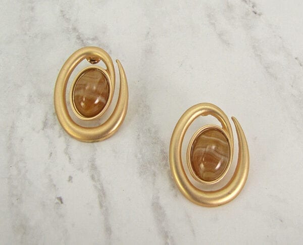 golden earrings with brown gemstone on the center on a marble surface