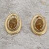 golden earrings with brown gem on the center on a concrete surface