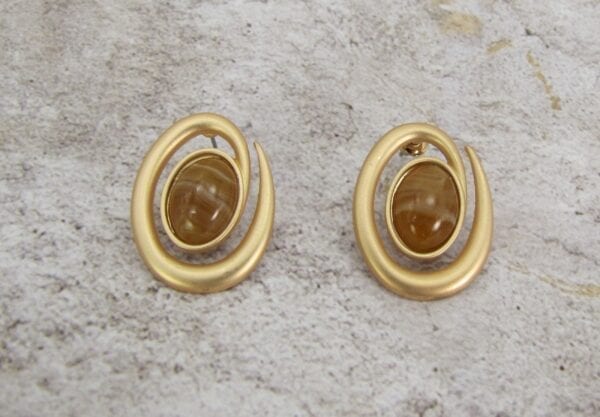 golden earrings with brown gem on the center on a concrete surface